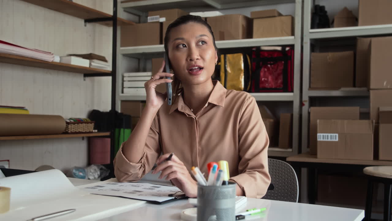 Asian Woman Accepting Clients Orders on Phone at Warehouse