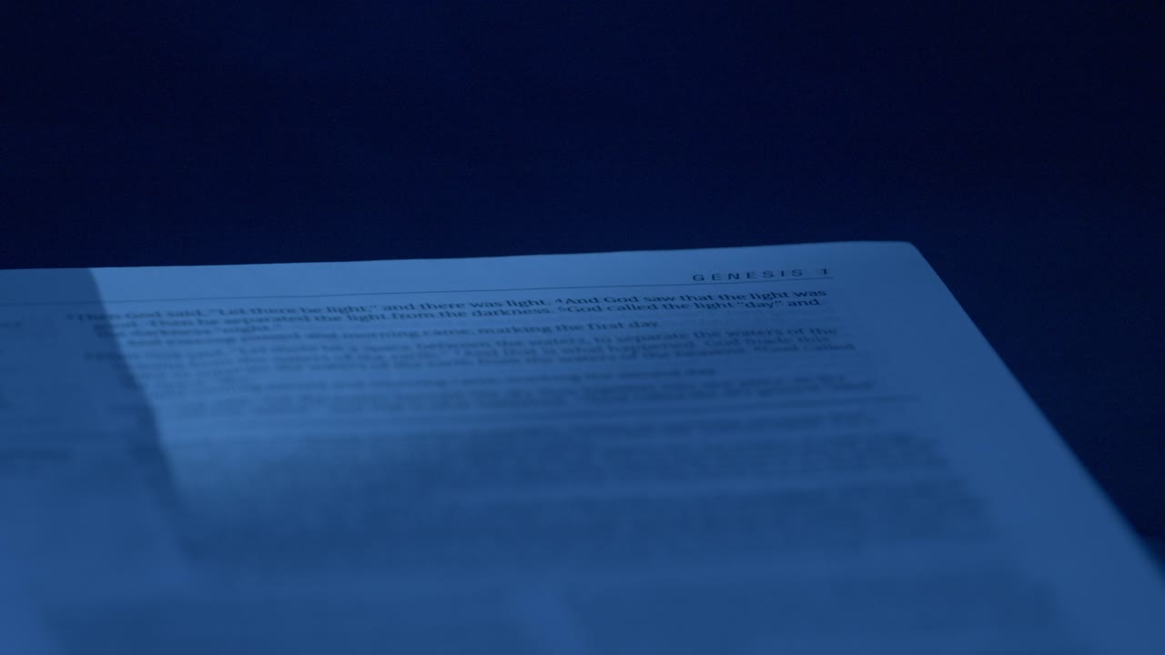 Close-up shot of a Bible page illuminated with dramatic blue lighting, highlighting text details. Captures an intimate, serene atmosphere, showcasing texture and composition vividly