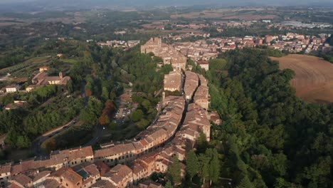 aerial drone view of a historic tuscan hill town with old buildings and narrow winding streets surrounded by dense forests and farmland. peaceful scene of heritage architecture in rural italy.