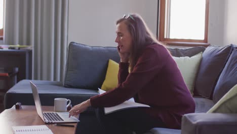 woman talking on smartphone while using laptop at home