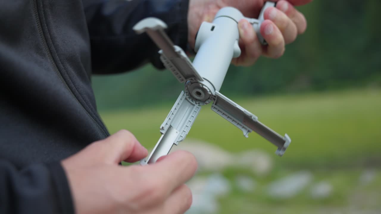 Hand Pulling Out Tripod Stand Of Insta360 Flow Pro AI Tracking Stabilizer. closeup shot