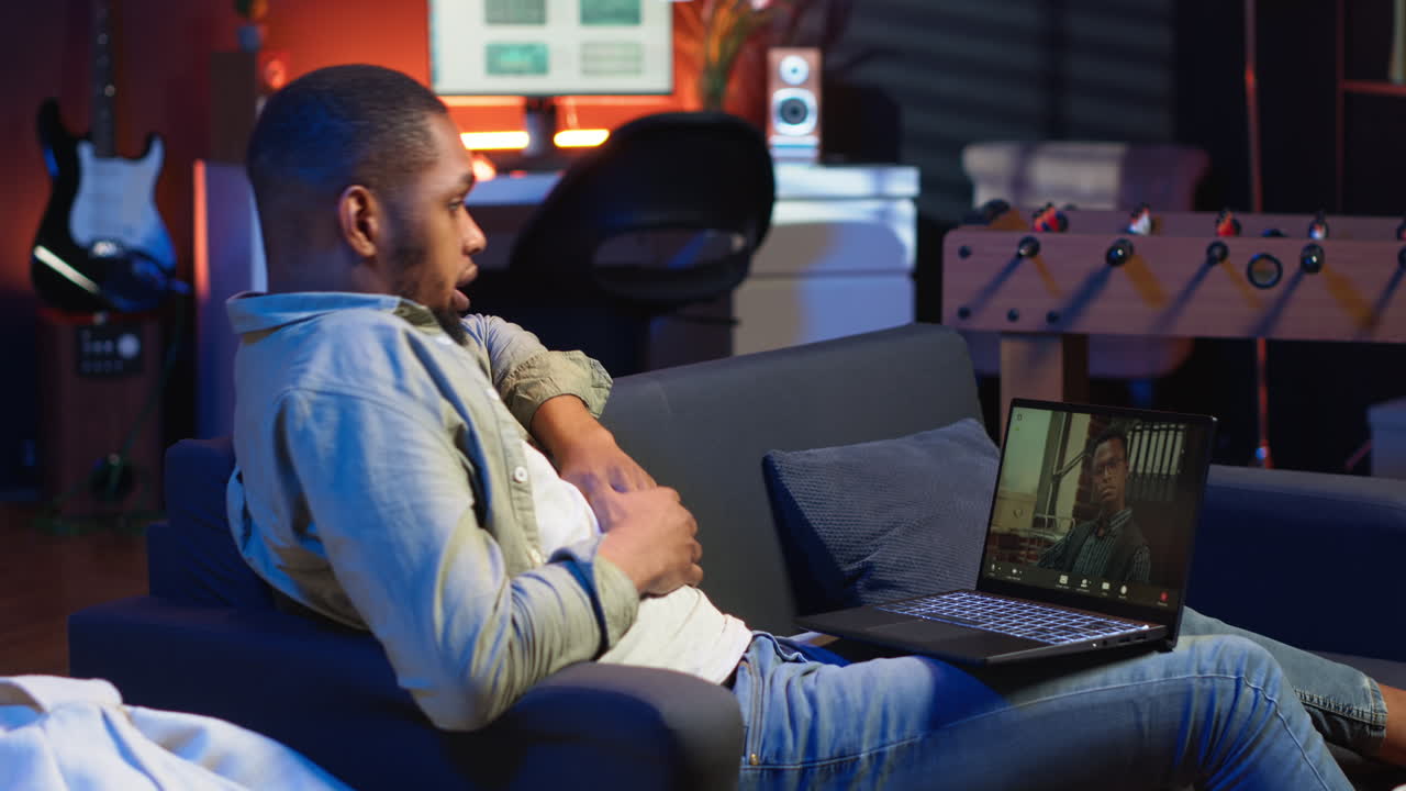 Focused black guy smiling and waving during a web conference in his living room