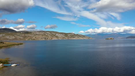 Beautiful-lake-of-Prespa-and-villages-on-shore,-calm-water-reflecting-mountains-and-clouds