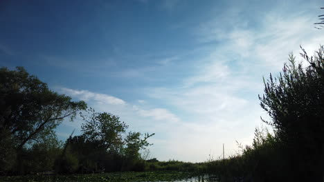 a motion time-lapse of the sky, fast moving clouds, and reveal of a summer pond during the daytime