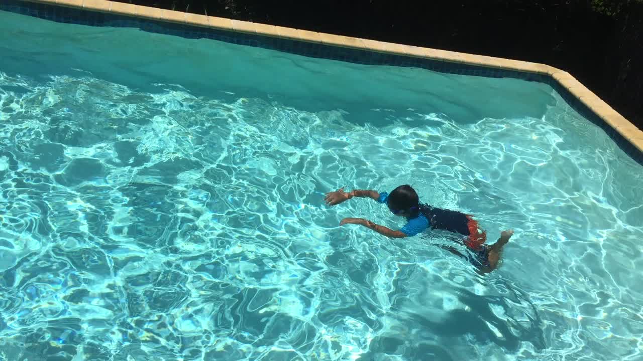 Anak laki-laki muda mendorong dirinya maju dengan gaya kupu-kupu di bawah air dari kanan ke kiri di kolam renang