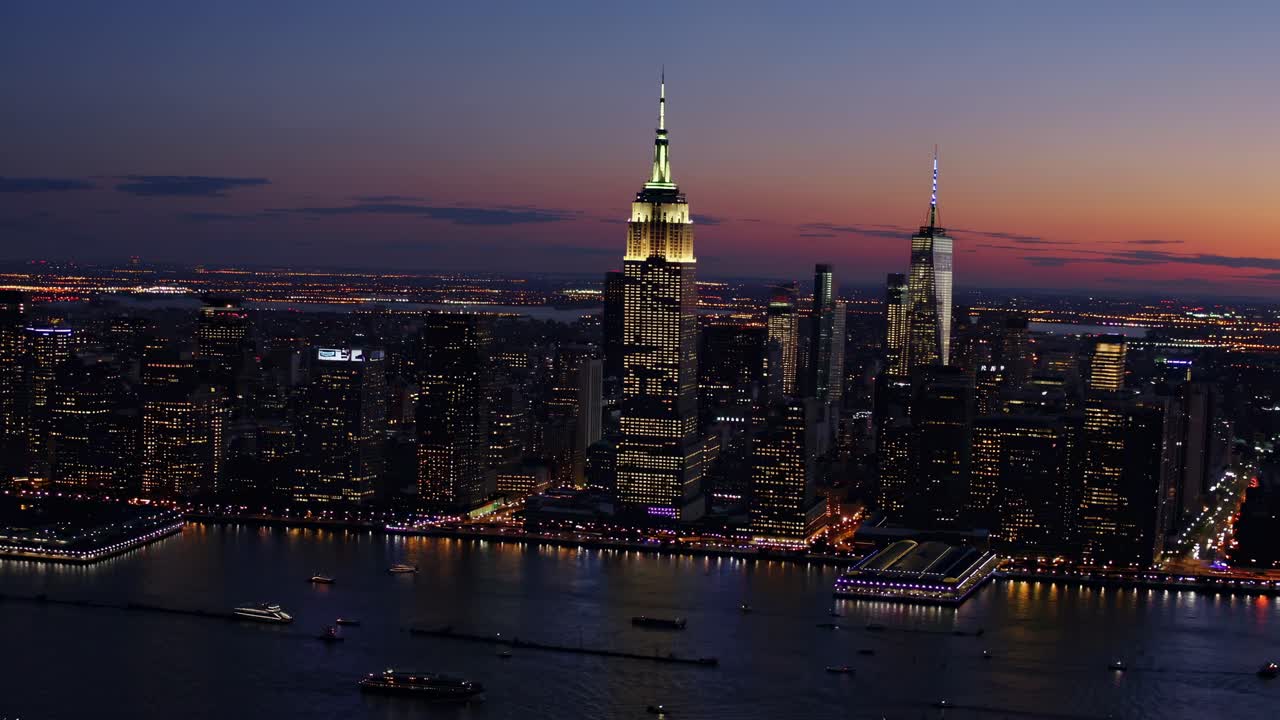 Aerial video captures a stunning cityscape at dusk, showcasing illuminated skyscrapers and a serene