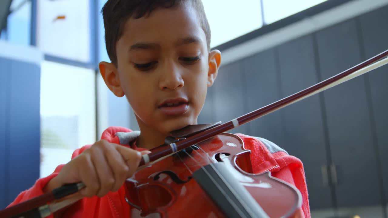 vista frontal de un escolar asiático atento tocando el violín en el aula de la escuela 4k