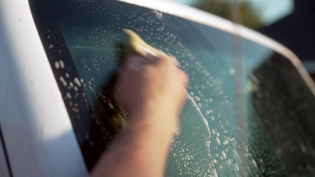 Hand scrubbing bugs off an SUV windshield during an exterior clean