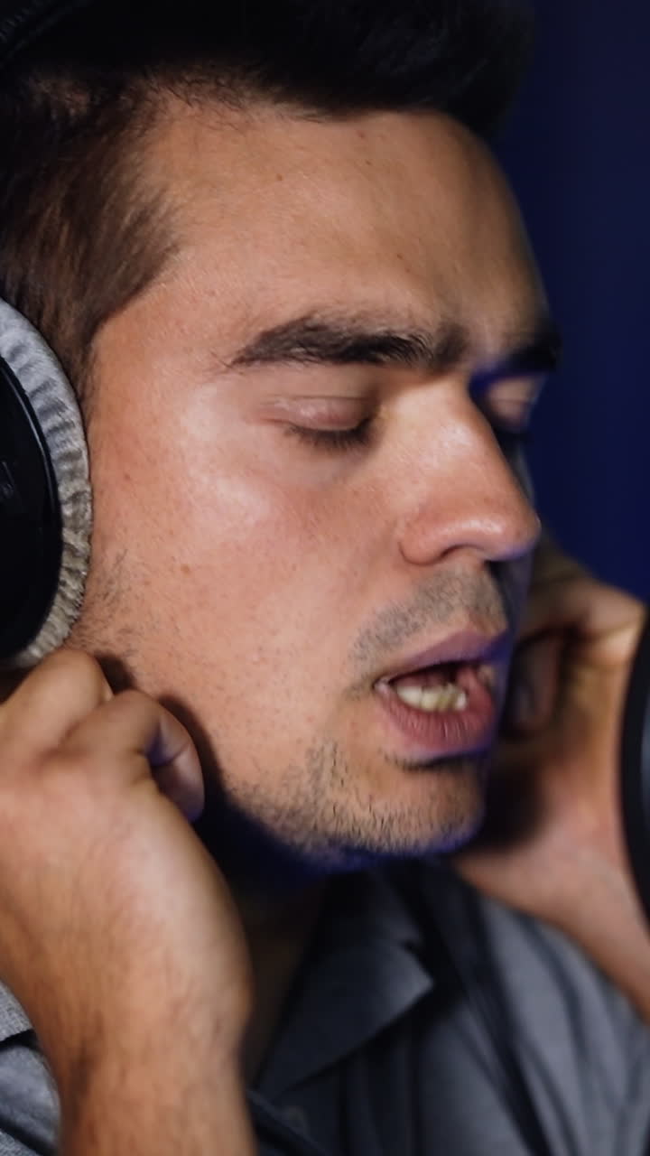 Recording a song in the professional studio. Portrait of a Caucasian male singer in headphones performing song. Close up. Vertical video