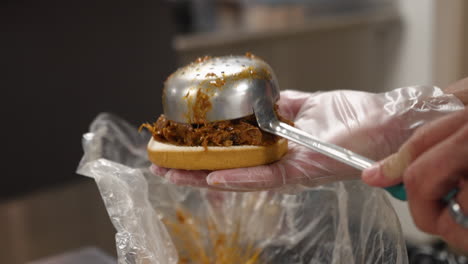 ladle carefully places rounded scoop of chopped beef brisket on bun for barbecue sandwich, slow motion close up 4k