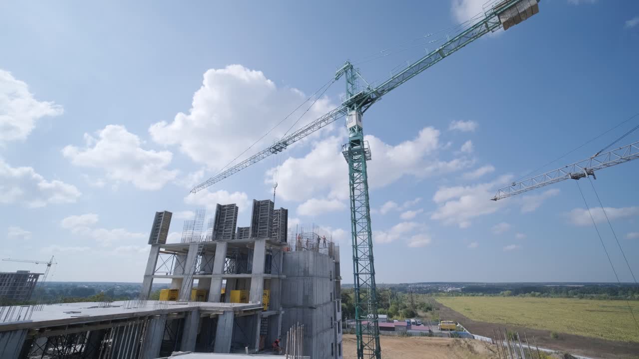 las grúas de torre trabajan en la construcción de edificios residenciales de ladrillo contra el fondo de un cielo azul.