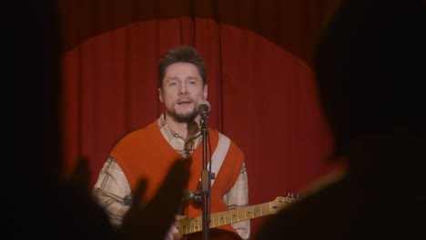 male musician thanking audience for applause and talking to them during a live music performance