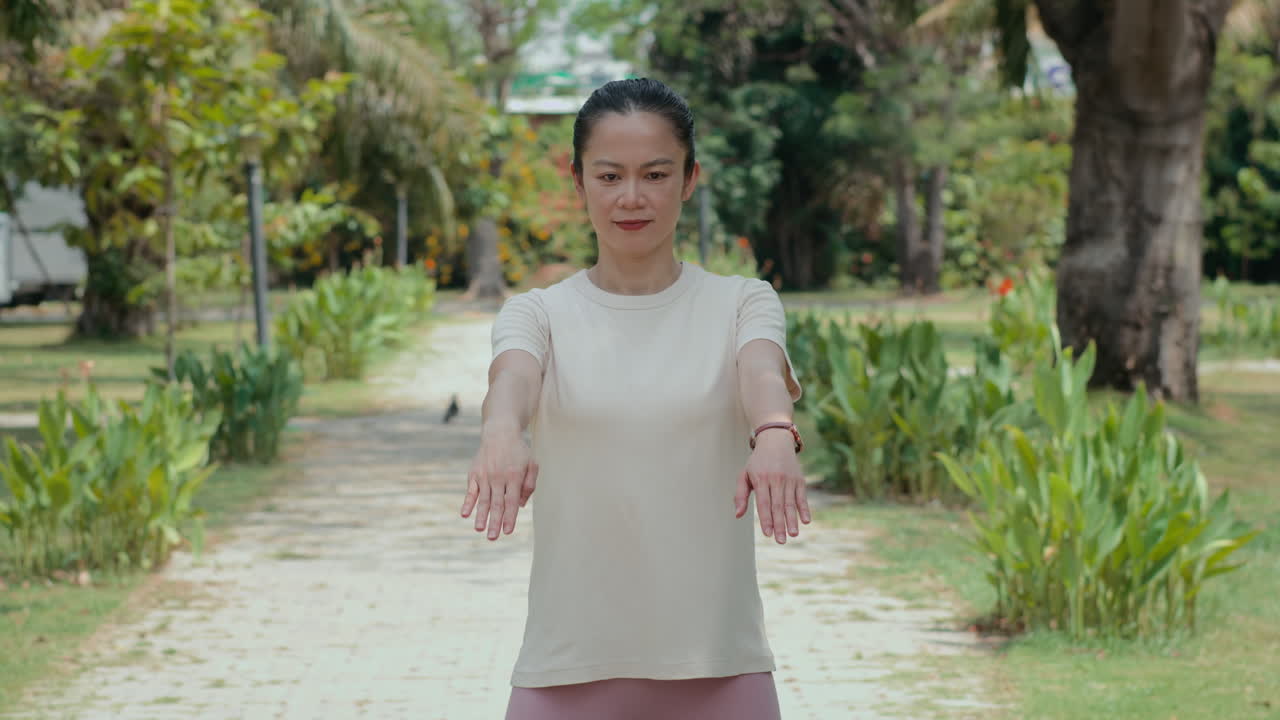 Middle-aged Asian Woman Practicing Arm Circle Moves at Local Park