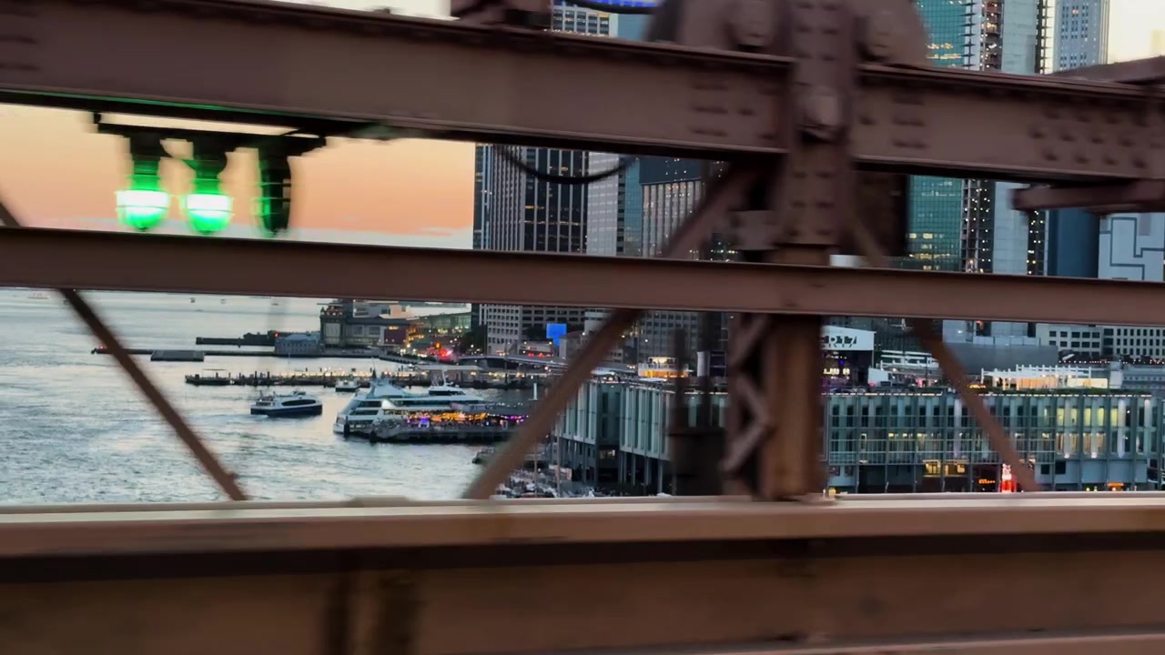 Vista dal Ponte di Brooklyn con barche sul fiume e edifici della città al tramonto.