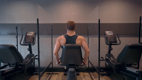 rear view of athletic man doing cardio cycling training in stationary bicycle machine at gym