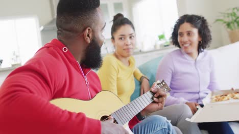 Happy,-diverse-female-and-male-friends-playing-guitar-and-listening-at-home-in-slow-motion