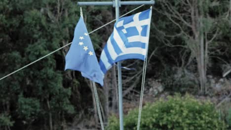 european union and greek flag hanging side by side waving in the wind with background of trees in kefalonia, greece