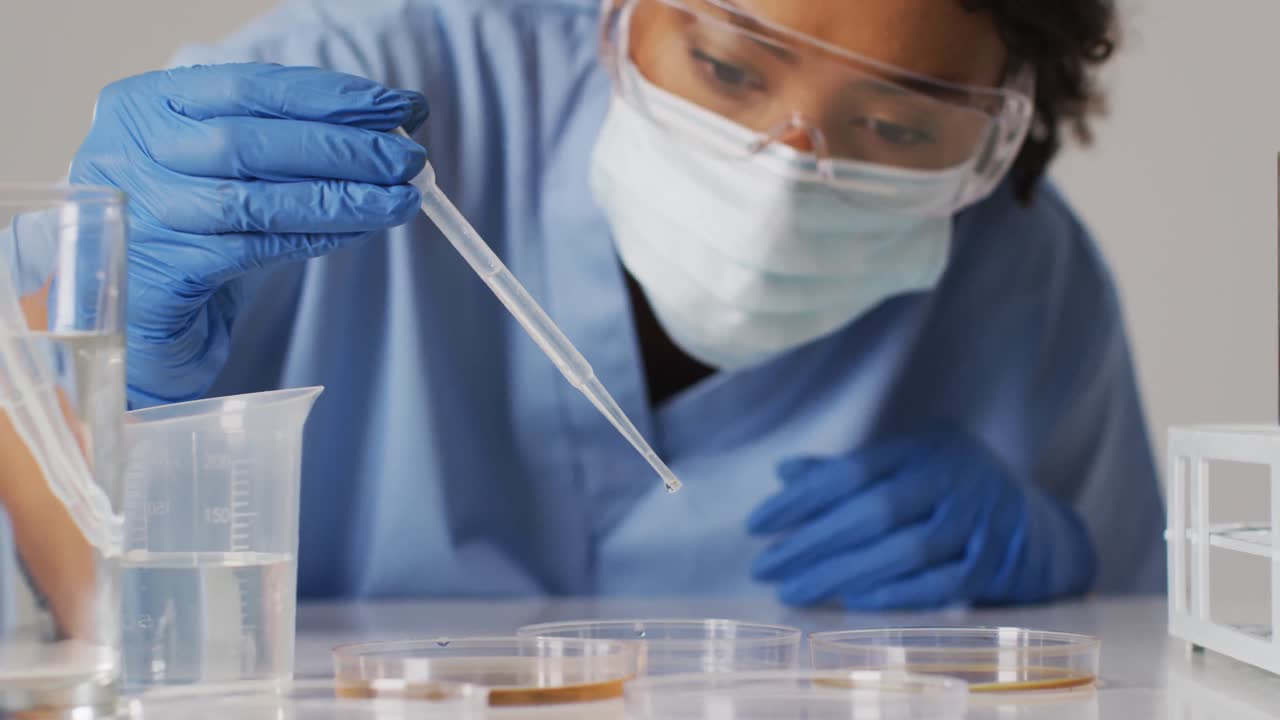 Video of biracial female doctor with face mask using pipette on blue background