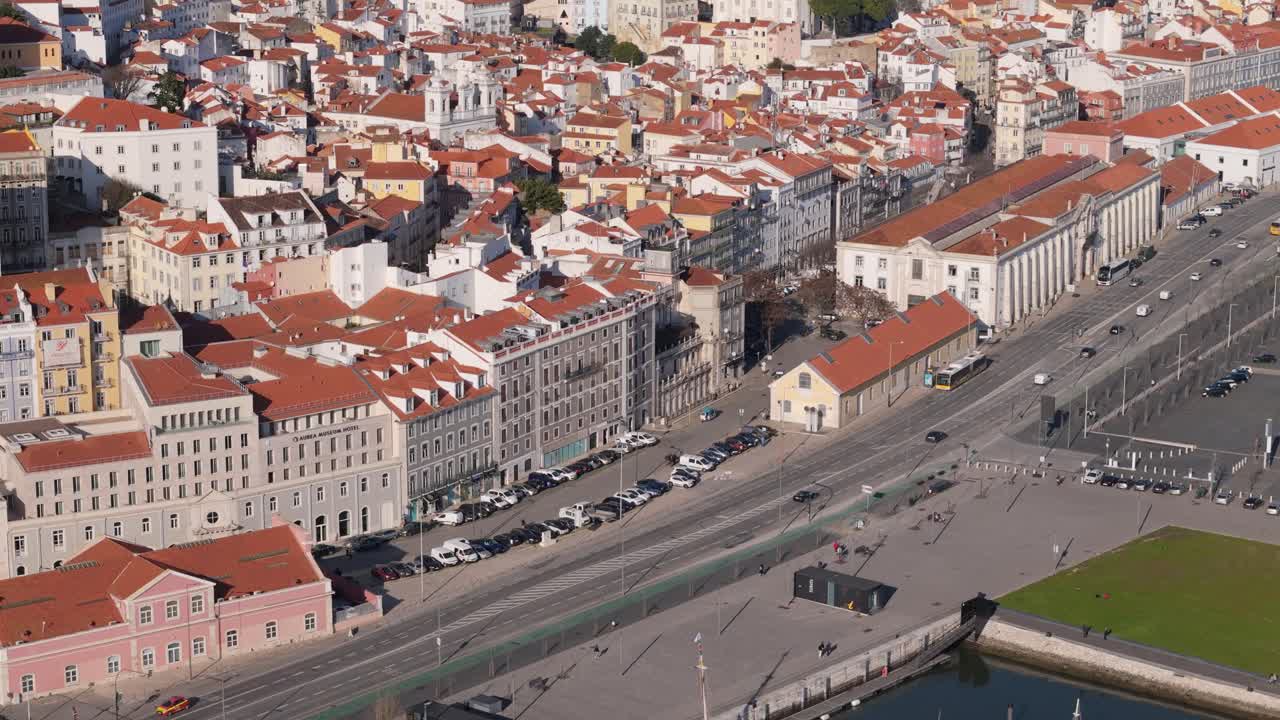 Ripresa aerea lungo una strada vicino al fiume Tago con auto che circolano a mezzogiorno sotto una cattedrale arancione e tetti di case a Lisbona, Portogallo.
