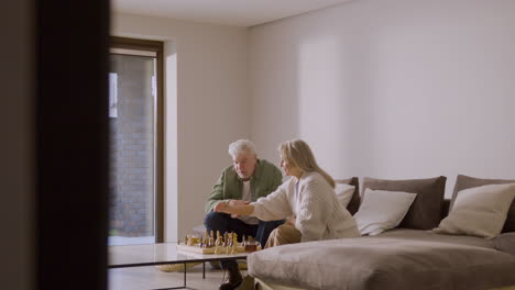 senior man and woman playing chess while sitting on sofa at home 3