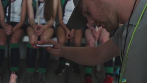 hockey coach explaining game plan with female players in locker room