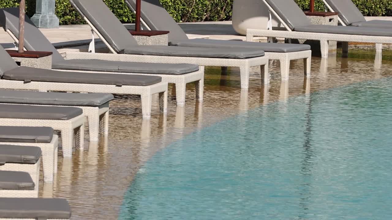 A serene view of sun loungers beside a clear, inviting pool under bright sunlight.