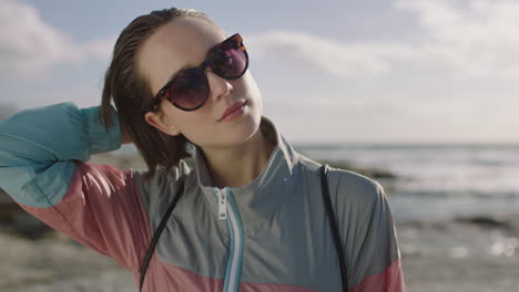 retrato de una mujer fresca tocando el cabello confiada en la playa con gafas de sol