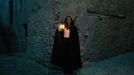 mysterious woman with lantern and cloak at night on a street of medieval city