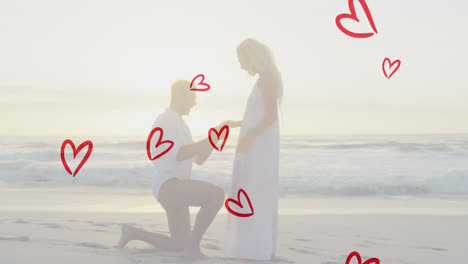 animation of red hearts over caucasian man proposing on beach