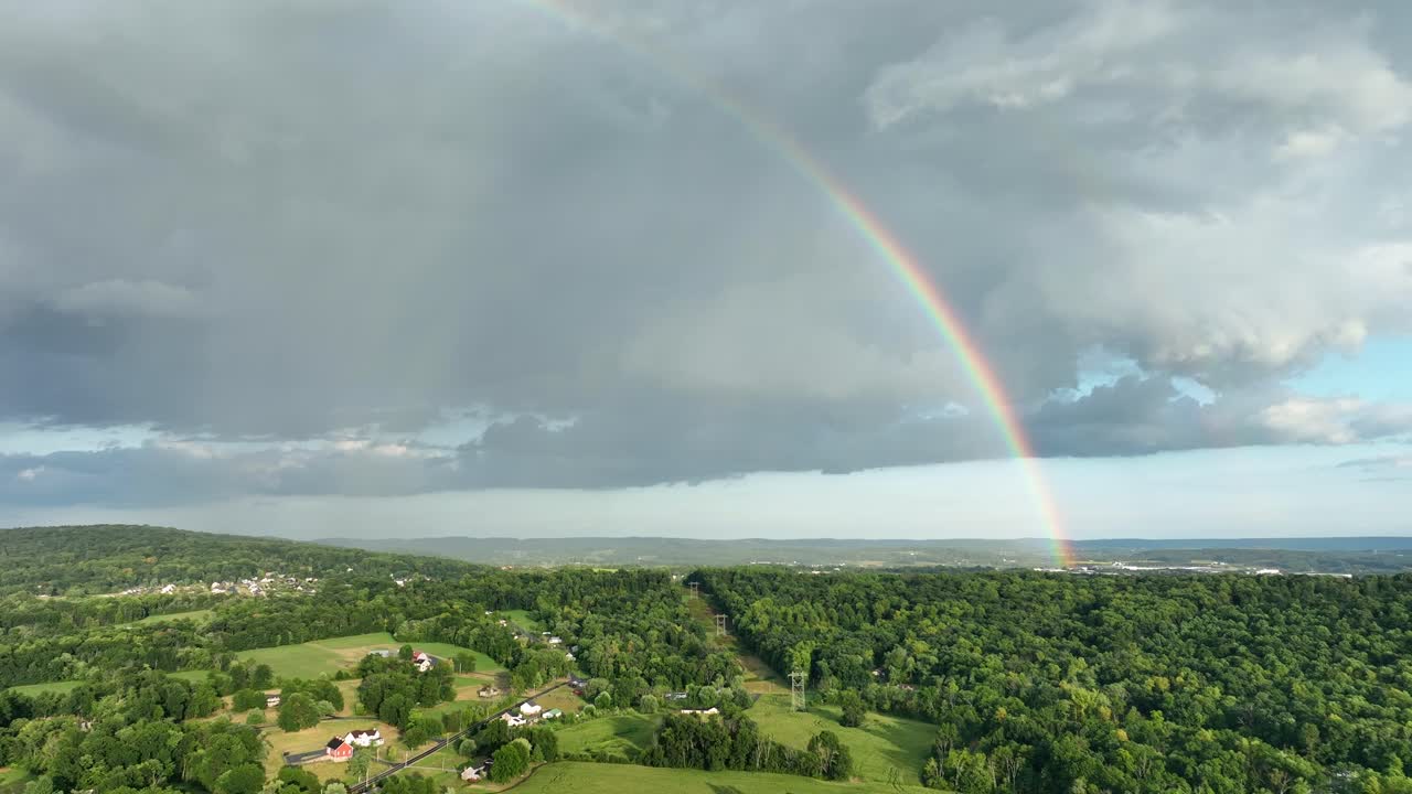 un vuelo aéreo sobre las tierras de cultivo rurales verdes después de una tormenta con las nubes y un arco iris en el cielo