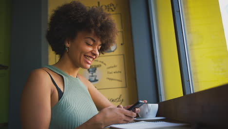 Cliente-Femenina-En-Mensajes-De-Ventana-De-Cafetería-Mediante-Teléfono-Móvil