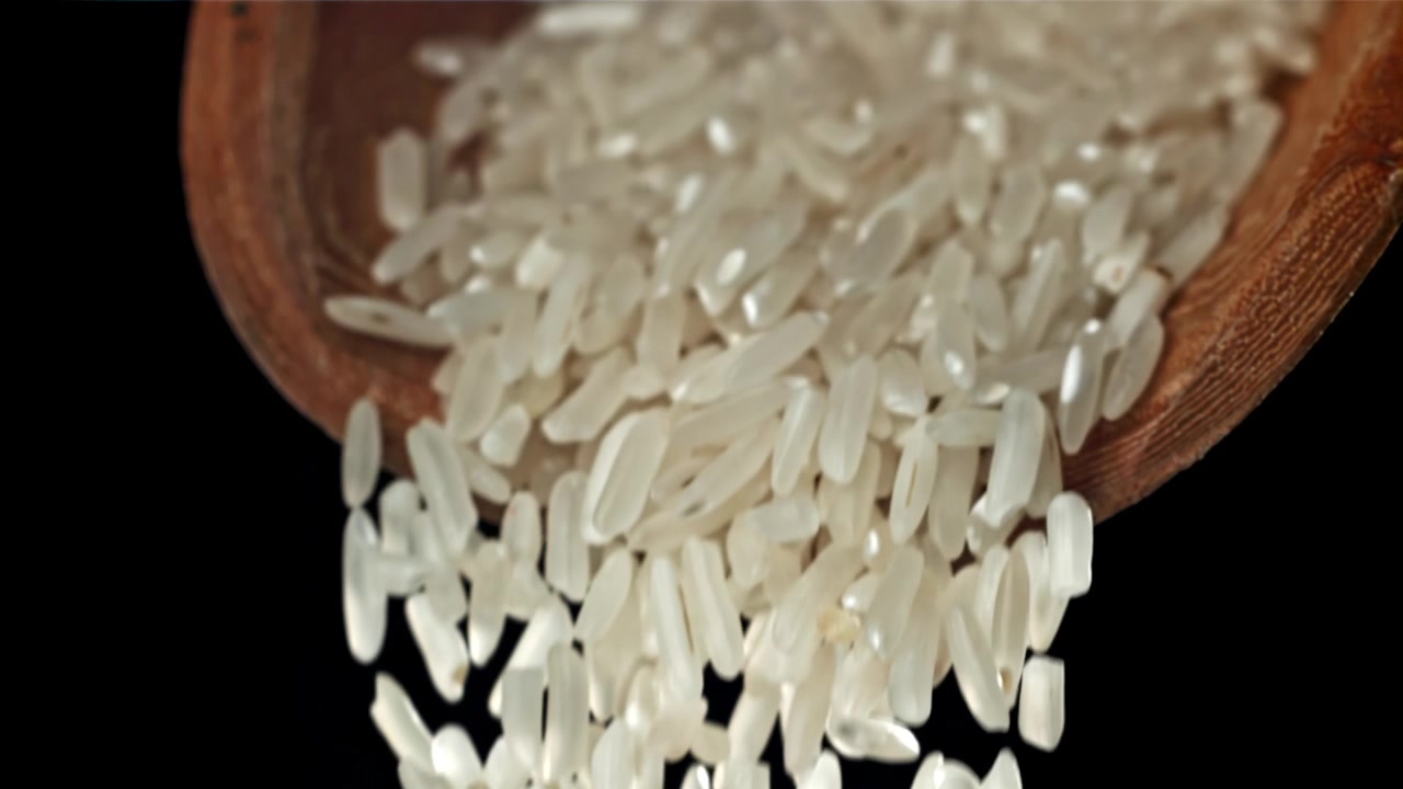 Chicchi di riso bianco che cadono da un cucchiaio di legno al rallentatore