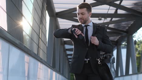a young businessman near the business center he looks at his wristwatch a young businessman near the business center he looks at his wristwatch the man walks and smiles business concept