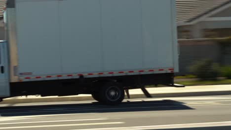 home moving and shipping company white box truck driving down a road to its destination in 4k - panning shot