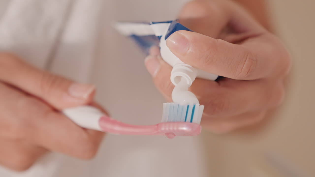 Huésped se cepilla los dientes. Huésped del hotel se cepilla los dientes rápidamente. Persona prepara cepillo y pasta dental para la rutina matutina. Huésped en el hotel se prepara cepillándose los dientes con el baño de fondo.