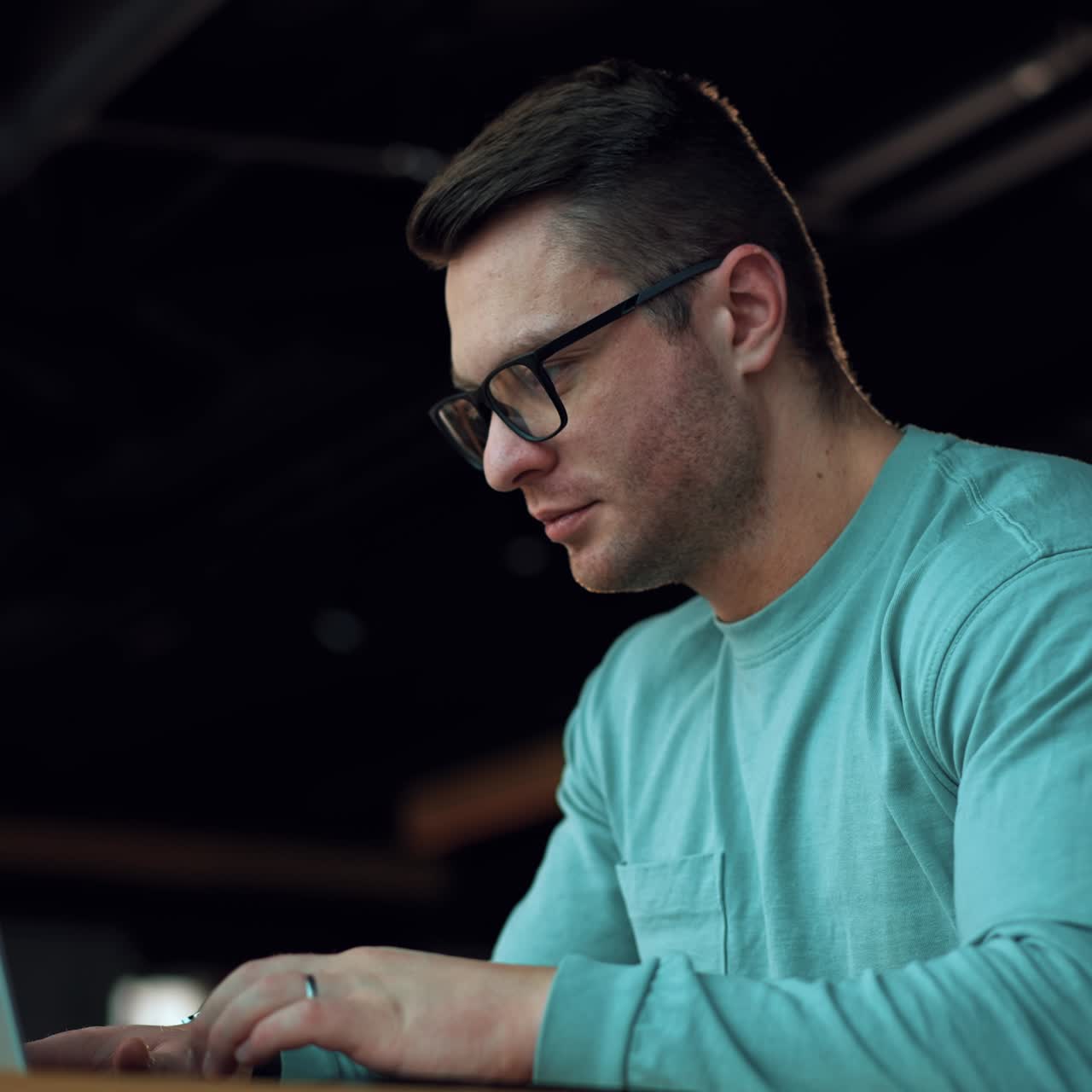 Dark-haired handsome man in glasses working on laptop. Businessman think of a job issue holding by his chin. Close up
