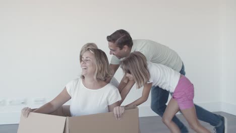 cheerful dad and two daughters dragging box with happy mother