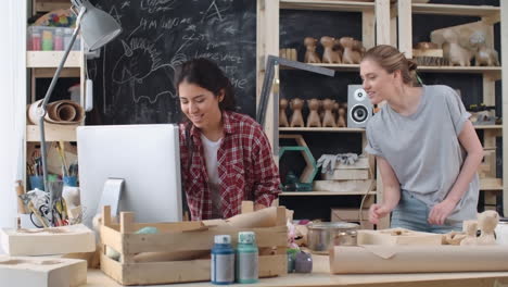 Dos-Mujeres-Artesanas-Se-Ríen-Y-Hablan-Mientras-Miran-La-Pantalla-De-La-Computadora-En-Un-Taller-Artesanal