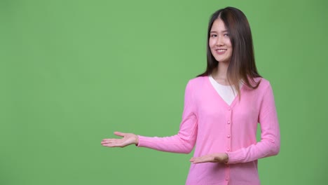 Young beautiful Asian woman showing something