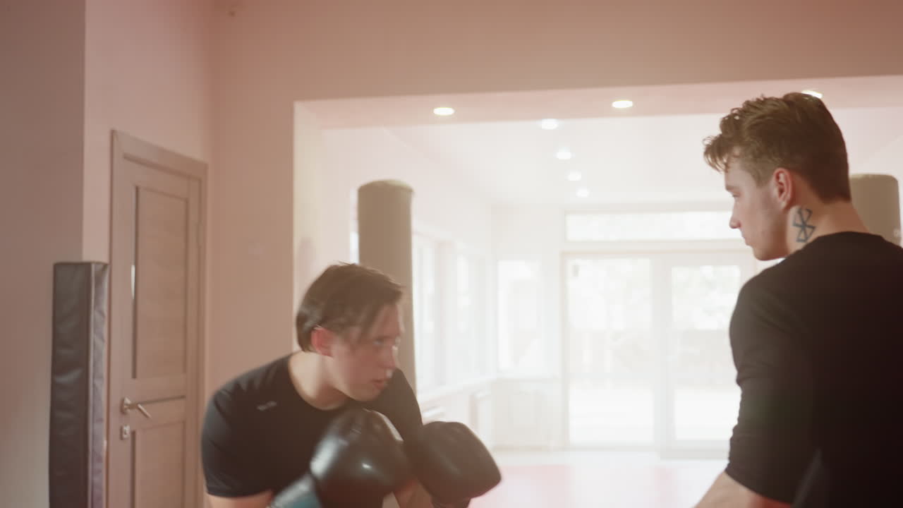 MMA fighter in black gloves trains with coach holding red mitt inside bright gym, showcasing discipline, power, endurance, and technique during intense combat practice session with focus and determination