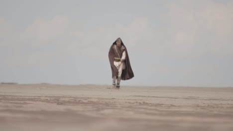 a robed figure struggles across a vast sand dune, then falls to their knees in exhaustion. post-apocalyptic, sci-fi, or fantasy concept of despair, struggle, and survival