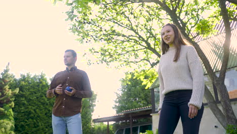 bottom view of caucasian young woman throwing a yellow petanque ball in the park on a sunny day while her male friend waits his turn