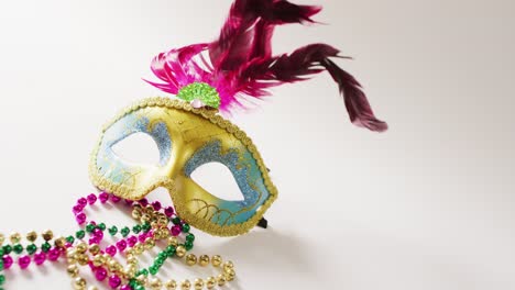 Video-of-masquerade-mask-with-pink-feathers-and-mardi-gras-beads-on-white-background-with-copy-space