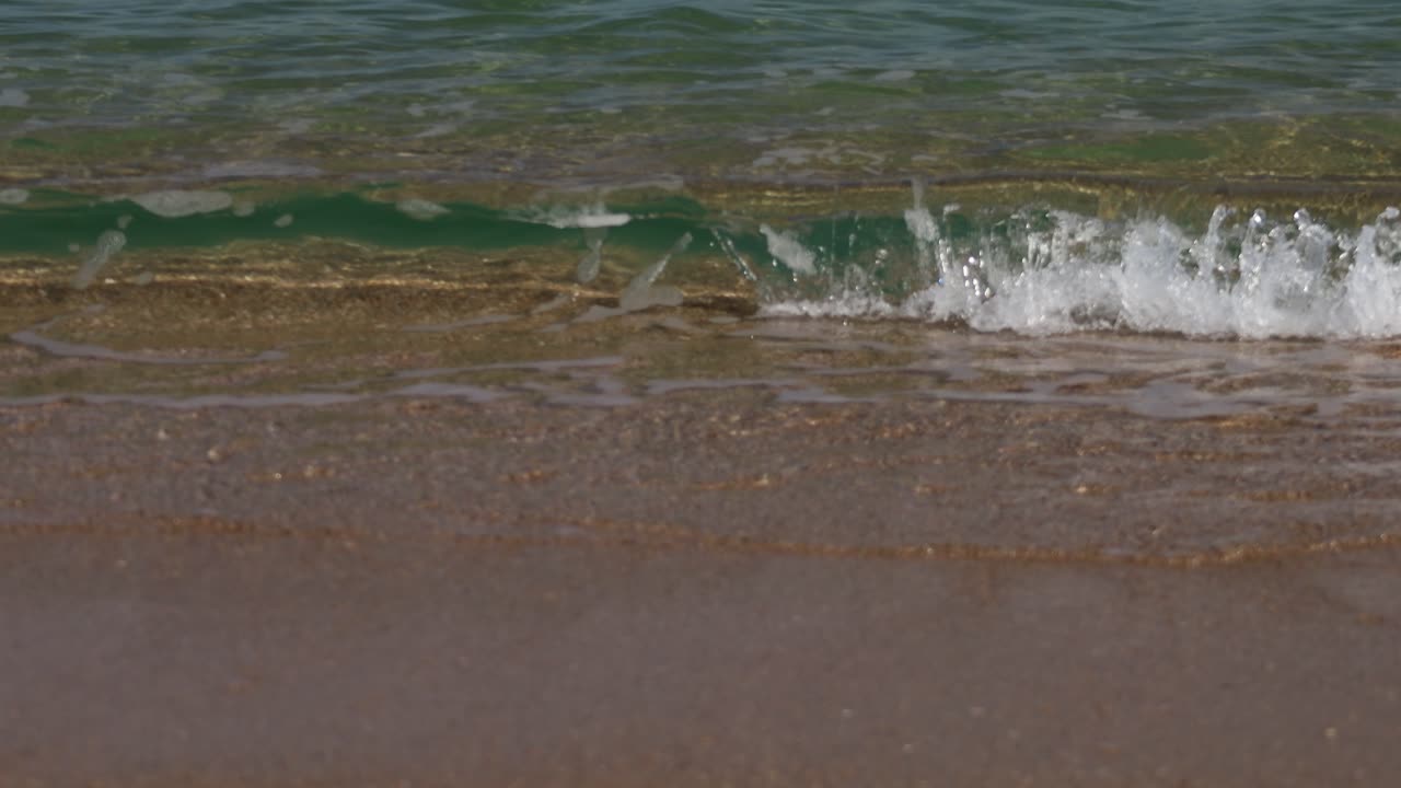 White ocean waves breaking on sandy coastline in bright sunny weather