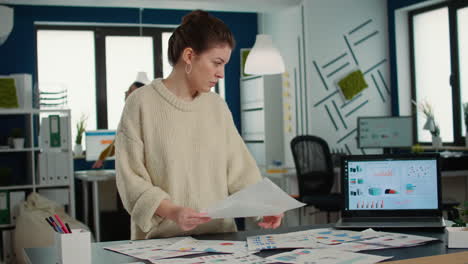 Portrait of busy startup employee holding papers with business charts comparing smiling at camera