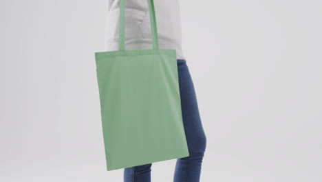mujer caucásica con capucha blanca sosteniendo una bolsa verde sobre fondo blanco, espacio de copia, cámara lenta