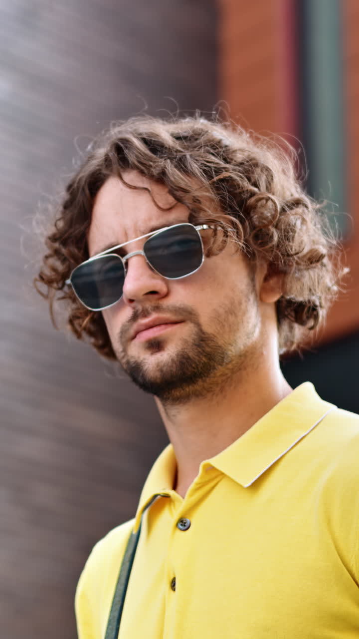Man wearing a yellow shirt and sunglasses standing with buildings on the background. Vertical