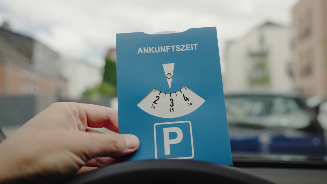 Un conducente tiene un disco orario tedesco con la parola Ankunftszeit (ora di arrivo) all'interno dell'auto prima di parcheggiare in una strada di città europea.