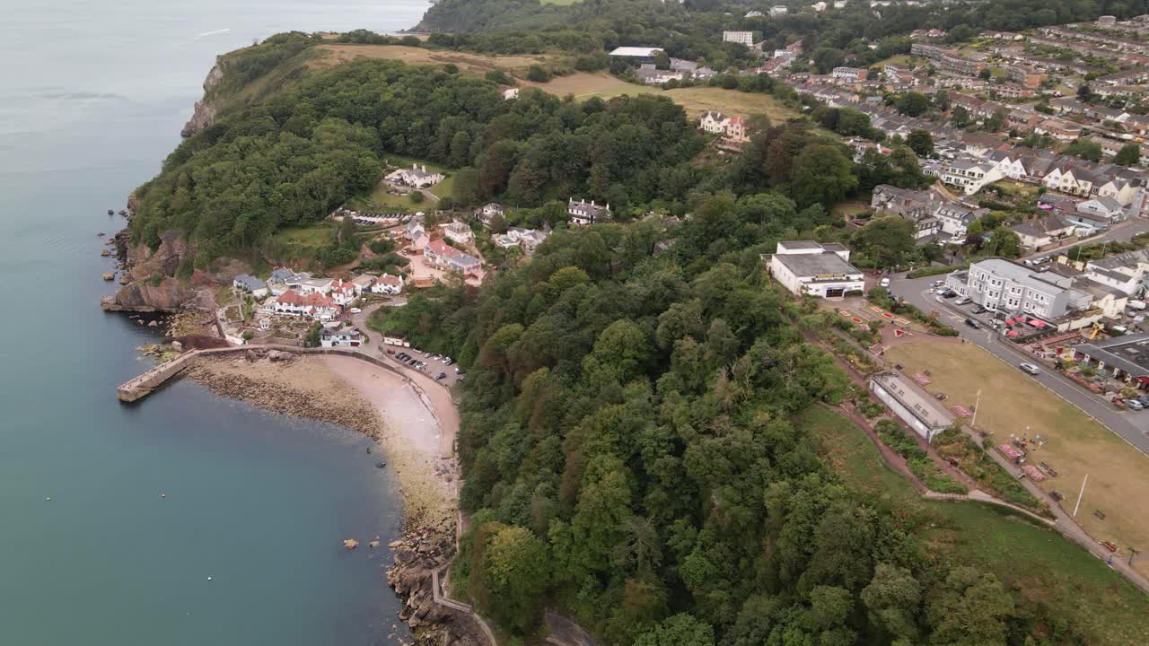 toma aérea del lado del carro de la playa de babbacombe, la costa, los acantilados cubiertos de maleza y la ciudad de torquay en la cima de la montaña