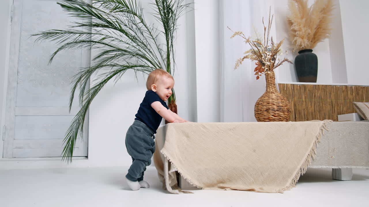 Cute smiling infant baby stands in the room. Adorable child trying to stand and walk alone.